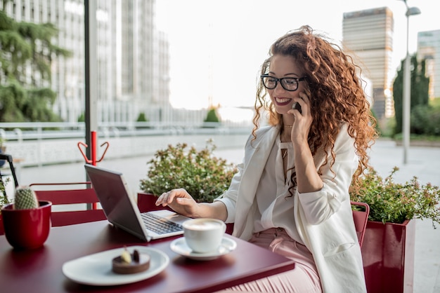 Jonge zakelijke roodharige vrouw op de computer en mobiele telefoon