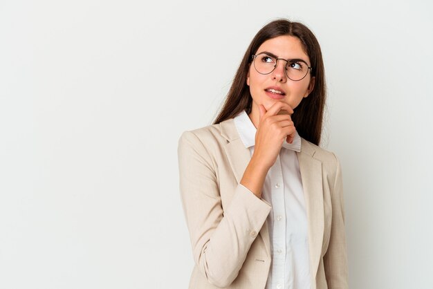 Jonge zaken blanke vrouw geïsoleerd op een witte muur opzij kijkt met twijfelachtige en sceptische uitdrukking