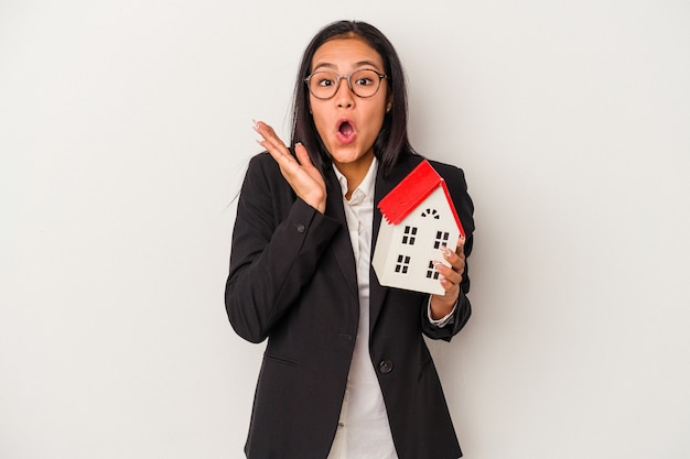 Jonge zaken Latijns-vrouw met een speelgoed huis geïsoleerd op een witte achtergrond verrast en geschokt.