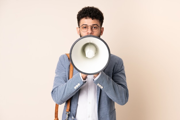 Jonge zaken Marokkaanse man geïsoleerd op beige achtergrond schreeuwen door een megafoon