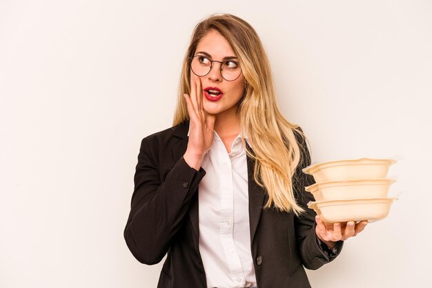 Jonge zakenkaukasische vrouw met tupperware geïsoleerd op een witte achtergrond zegt een geheim heet remnieuws en kijkt opzij