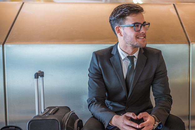 Jonge zakenman bij luchthaven glimlachen die op zijn vlucht met bagage wachten