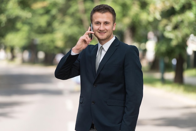 Jonge zakenman die aan de telefoon praat terwijl hij buiten staat in ParkxA