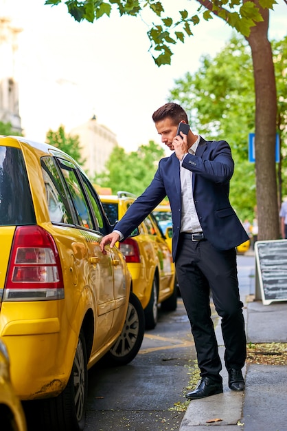 Foto jonge zakenman die aan een taxi loopt en op een telefoon spreekt