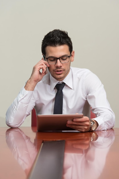 Jonge zakenman die aan zijn tablet werkt terwijl hij aan de telefoon praat