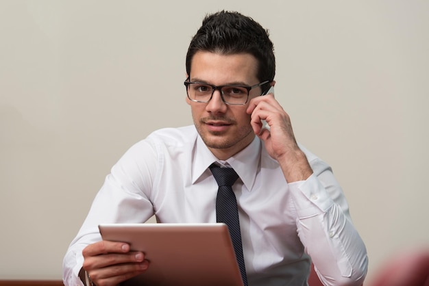 Jonge zakenman die aan zijn tablet werkt terwijl hij aan de telefoon praat