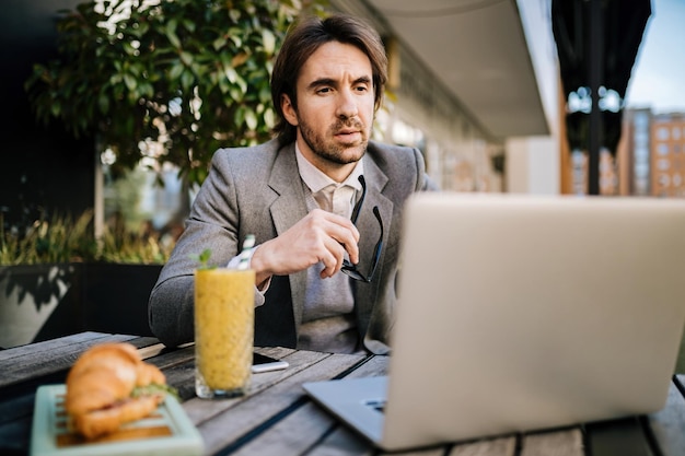 Jonge zakenman die een e-mail leest op laptop terwijl hij in een café op de stoep zit.