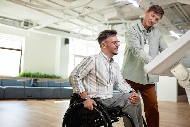 Jonge zakenman die een gehandicapte man helpt met behulp van een assistentcomputer