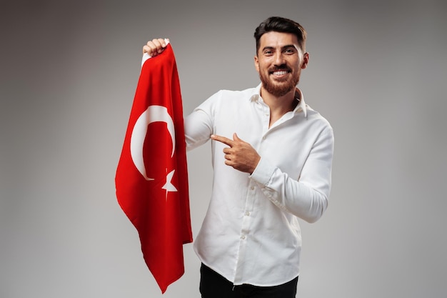 Jonge zakenman die een vlag van Turkije op grijze achtergrond houdt