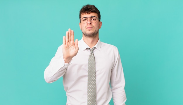 Jonge zakenman die er serieus, streng, ontevreden en boos uitziet en een open palm laat zien die een stopgebaar maakt