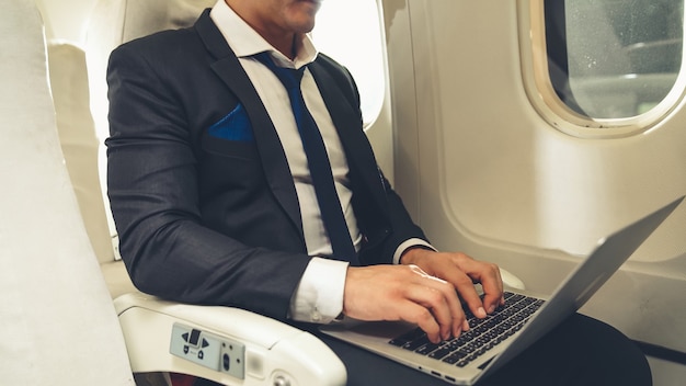 Jonge zakenman die laptopcomputer in vliegtuig met behulp van