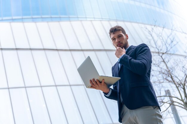 Jonge zakenman die met een computer in een glazen bouwconcept financiën kijkt