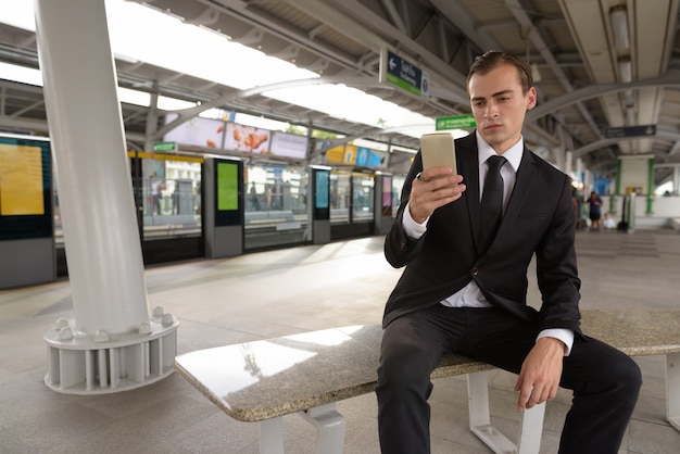 Jonge zakenman die mobiele telefoon met behulp van bij treinstation