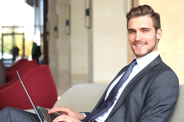 Jonge zakenman die op laptop werkt en in de lobby van het hotel op iemand wacht