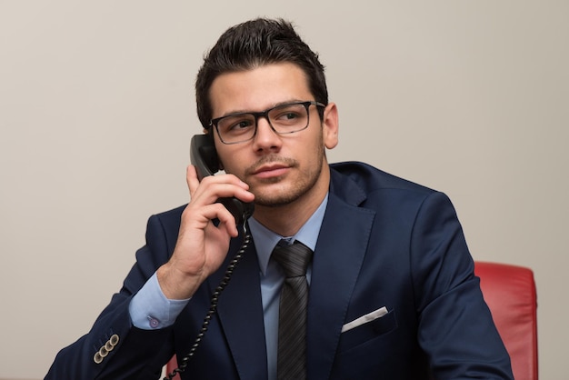 Jonge zakenman die op zijn computer werkt terwijl hij aan de telefoon praat