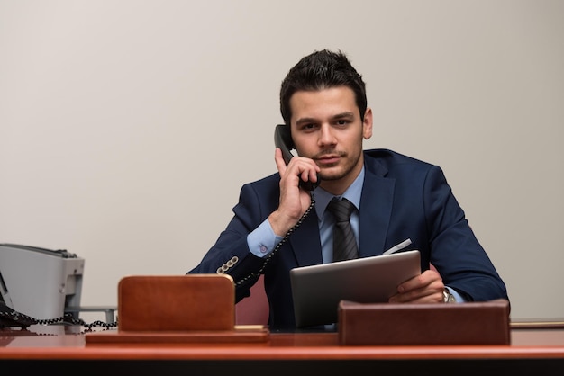 Jonge zakenman die op zijn computer werkt terwijl hij aan de telefoon praat