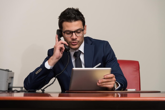 Jonge zakenman die op zijn computer werkt terwijl hij aan de telefoon praat