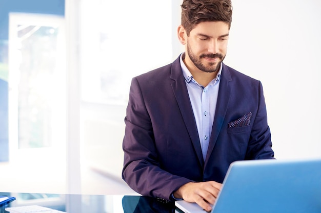 Jonge zakenman die zijn notebook gebruikt terwijl hij aan een bureau zit