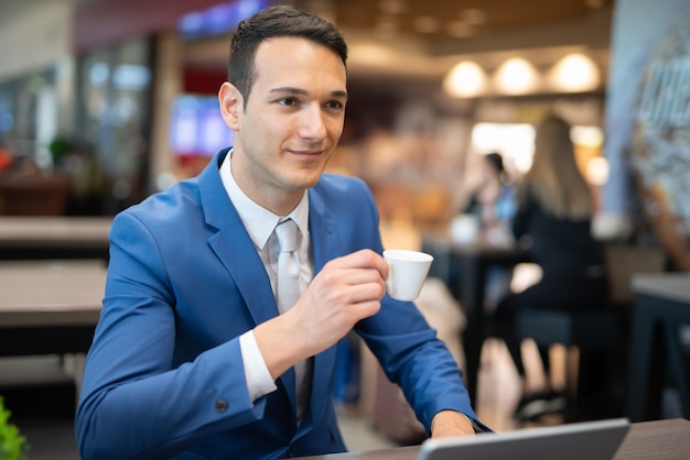 Jonge zakenman een kopje koffie drinken tijdens het werken op zijn laptop