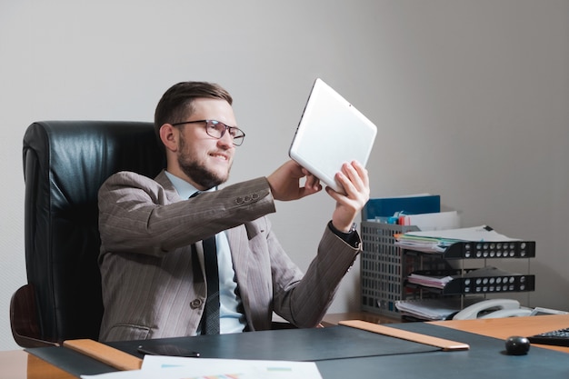 Jonge zakenman in glazen die aan een tablet in zijn persoonlijk bureau werken