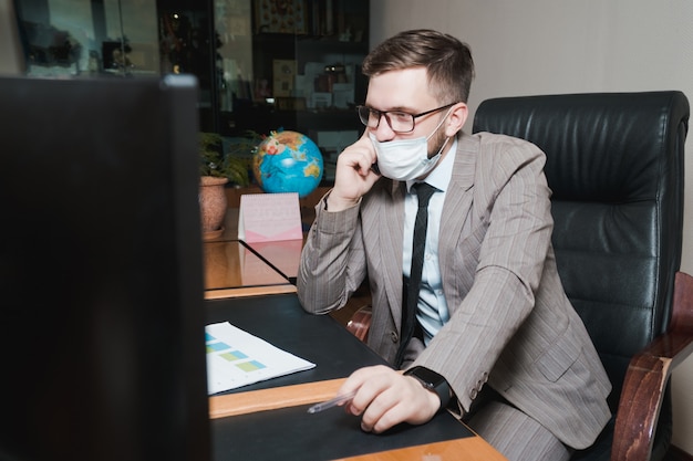 Jonge zakenman in glazen en gezichtsmasker in bureau