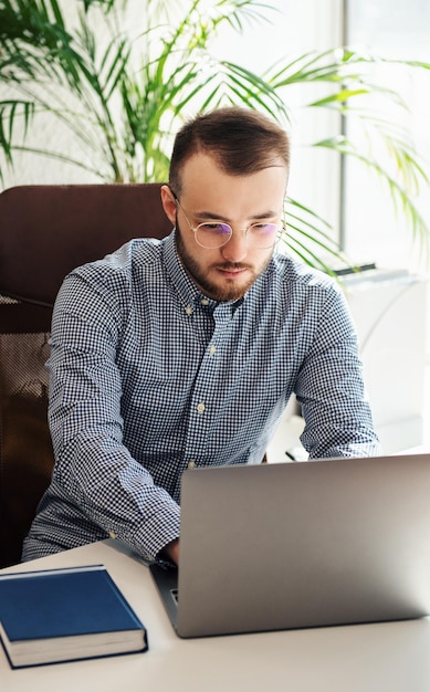 Jonge zakenman in overhemd die aan zijn laptop in een bureau werkt