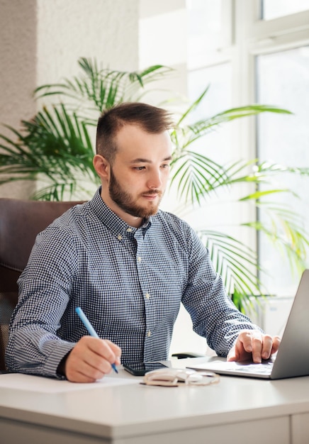 Jonge zakenman in overhemd die aan zijn laptop in een bureau werkt