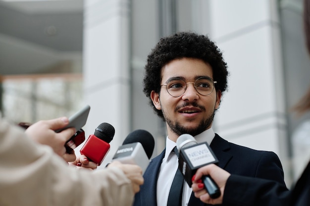 Foto jonge zakenman in pak die optreedt op zakelijke conferentie en toespraak houdt voor microfoons van repo