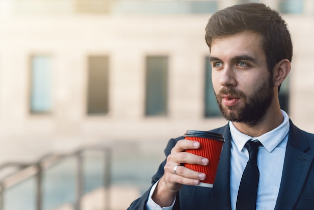 Jonge zakenman in pak houdt in de hand een rode papieren kopje koffie