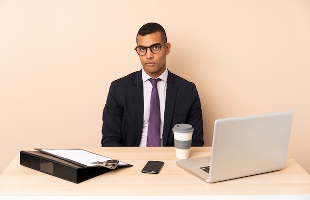 Jonge zakenman in zijn kantoor met een laptop en andere documenten met droevige en depressieve uitdrukking