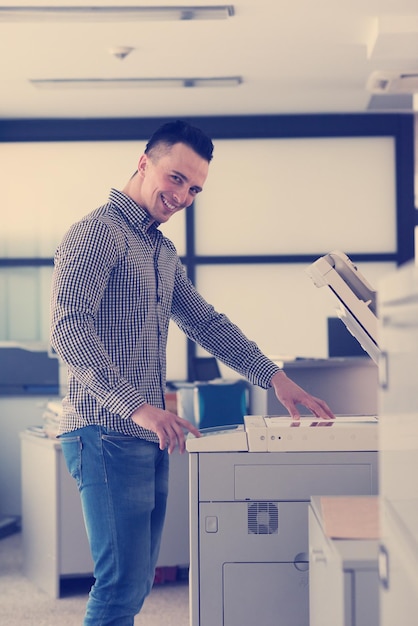 jonge zakenman kopieert documenten op kopieermachine bij modern opstarten kantoorinterieur, vrijetijdskleding