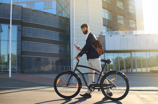 Jonge zakenman met beschermend masker met fiets en smartphone op straat in de stad.