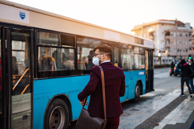Jonge zakenman met beschermend masker staat alleen op lege straat en wacht op bus of taxi. Virus pandemie of vervuiling concept.