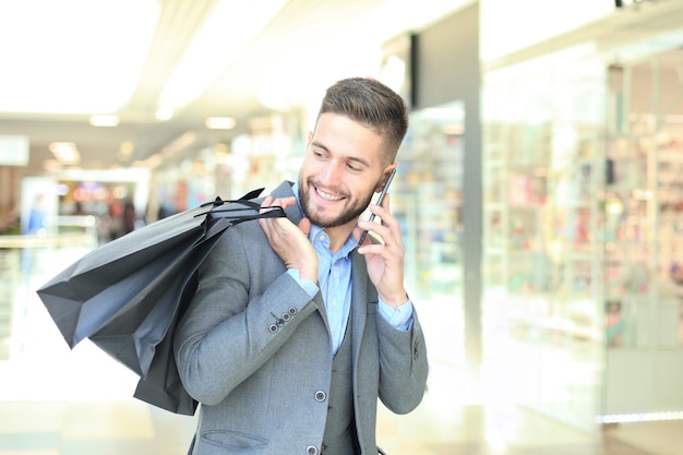 Jonge zakenman met boodschappentas praten aan de telefoon binnenshuis.