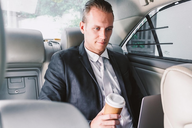Foto jonge zakenman met een laptop terwijl hij koffie drinkt in de auto