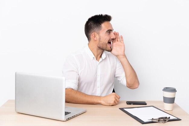 Jonge zakenman met een mobiele telefoon op een werkplek met wijd open mond schreeuwen