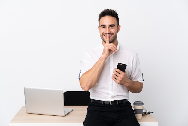 Jonge zakenman met een mobiele telefoon op een werkplek stilte gebaar doen