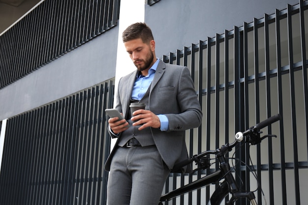 Jonge zakenman met fiets en smartphone op straat in de stad.