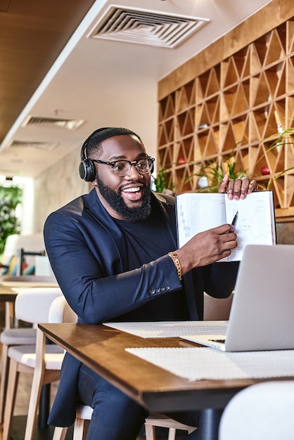 Jonge zakenman met koptelefoon zittend in café voor laptop en netwerken