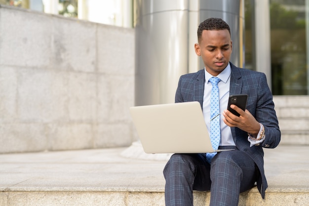 Jonge zakenman met laptop en telefoon zittend op de trap buiten