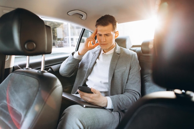 Jonge zakenman moe van het werk terwijl hij zijn hand op zijn hoofd houdt terwijl hij op de achterbank van de auto zit