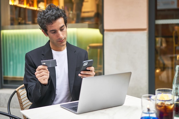 Jonge zakenman multitasking met online winkelen in een bar met behulp van technologie