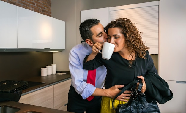 Jonge zakenman omhelst en kust een gelukkige gekrulde vrouw terwijl hij een snelle kop koffie drinkt voordat hij naar zijn werk gaat