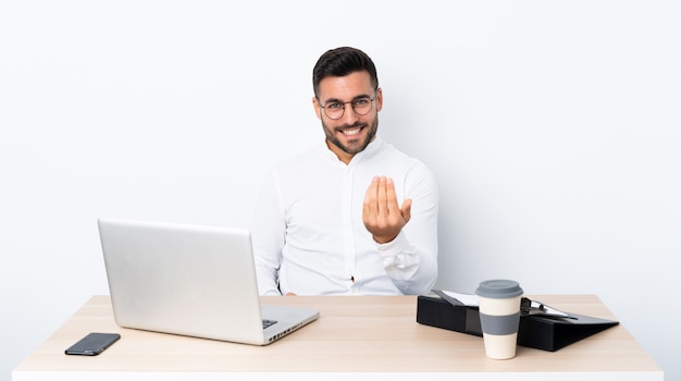 Jonge zakenman op een werkplek die met hand uitnodigt te komen. Blij dat je bent gekomen