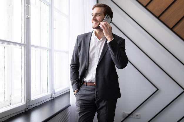 Jonge zakenman praten op een mobiele telefoon kijkt uit het raam op kantoor