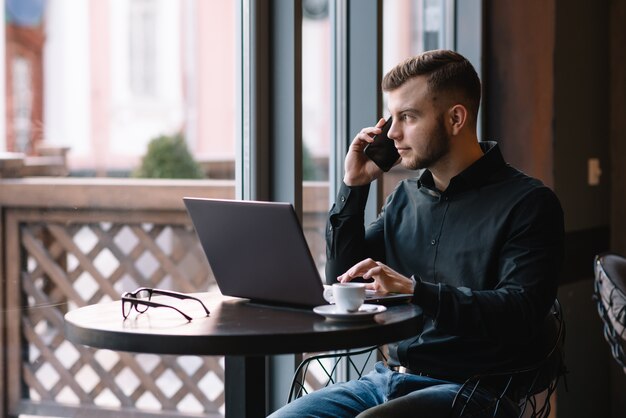 Jonge zakenman praten op mobiele telefoon tijdens het werken op laptop in café