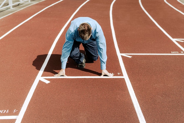 Foto jonge zakenman staat in start pose klaar om te rennen. een bedrijf starten. begin van een carrière. een kantoormedewerker traint in het stadion.