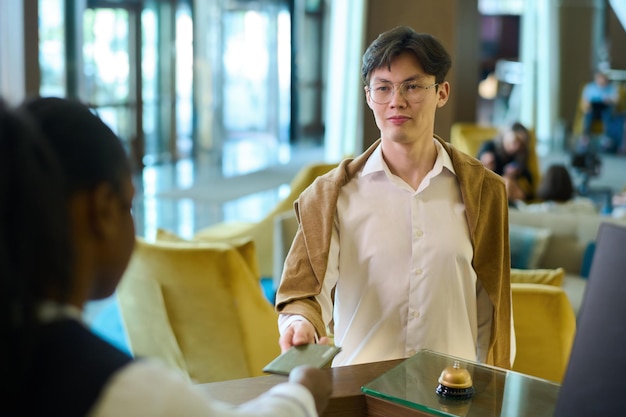 Jonge zakenman van Aziatische etniciteit geeft zijn paspoort door aan receptioniste
