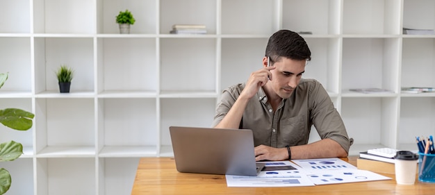 Jonge zakenman zit en controleert financiële documenten weergegeven in grafiekformaat, jonge zakenman die een startend bedrijf heeft opgericht en een nieuw bedrijf heeft geleid om met grote sprongen te groeien.