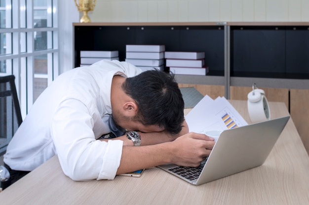 Jonge zakenmanslaap en overwerkt dichtbij laptop op kantoor.